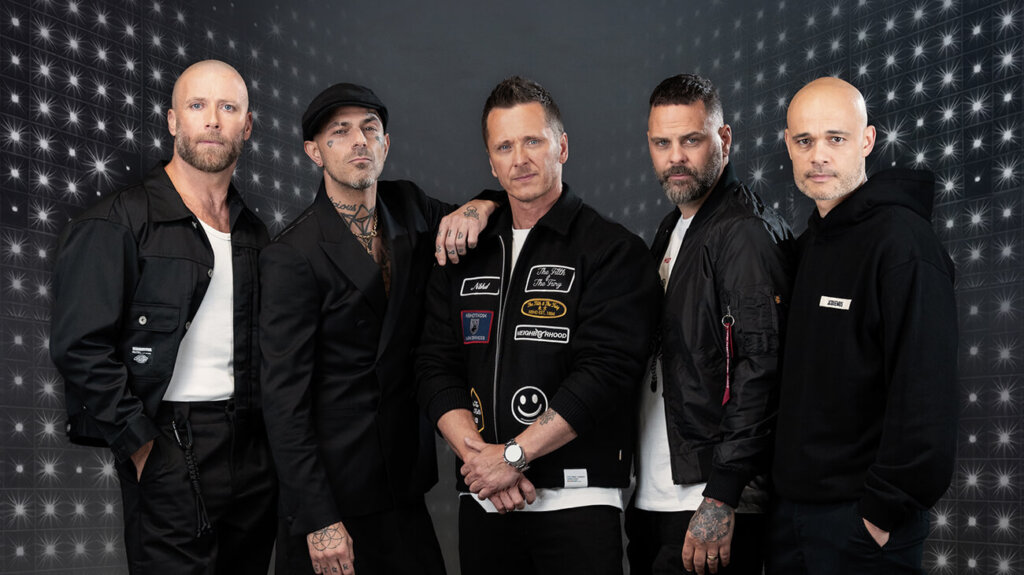 Five band members in black jackets standing closely together, posing for a photo.