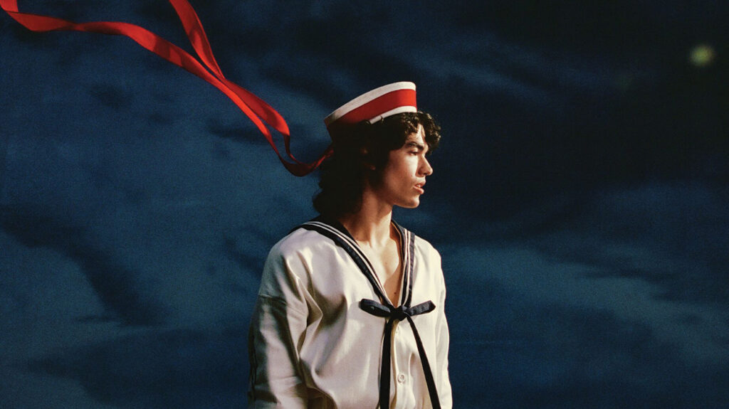 Singer Conan Gray in a sailors uniform posing against a clouded background.