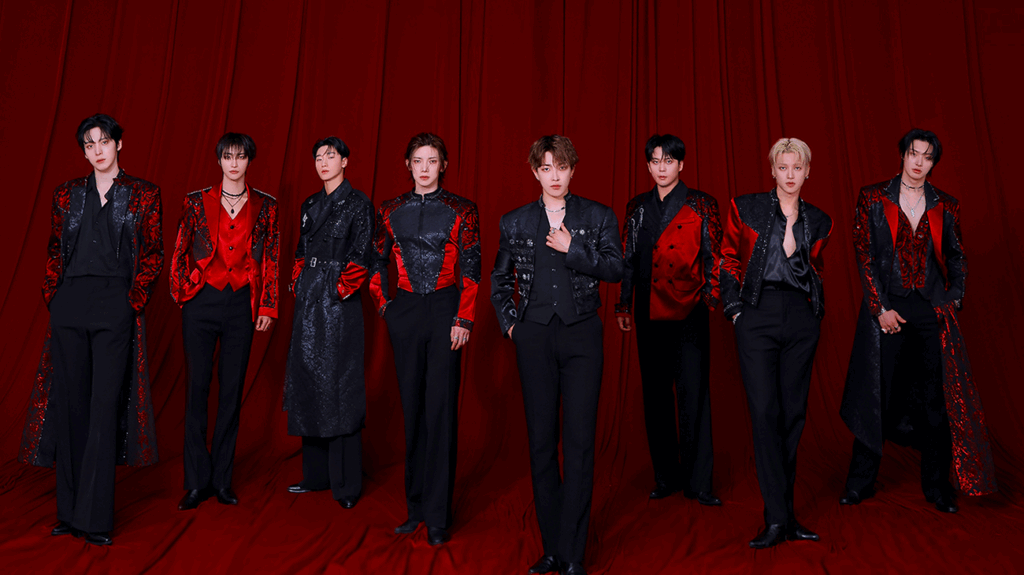 ATEEZ band members dressed in suits posing against a red draped background.