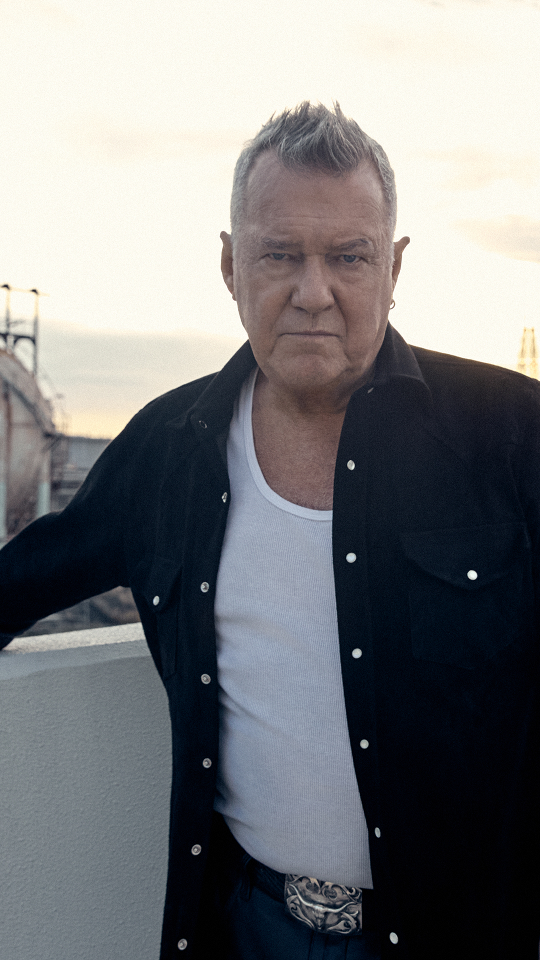 Singer Jimmy Barnes dressed in casual clothing posing against an industrial background.
