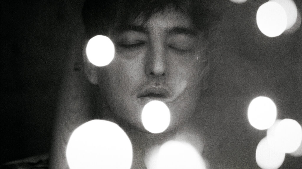 A close-up of singer Joji with his eyes closed, illuminated by a soft light.