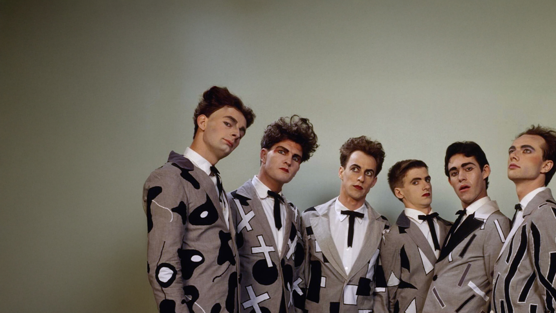 Members of the band Split Enz, dressed in suits, standing together and smiling for a group photo.