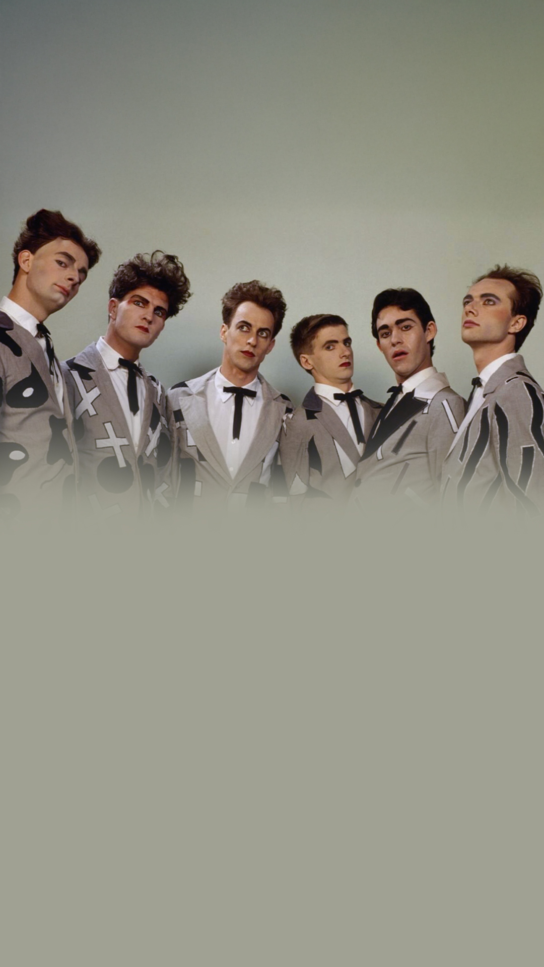 Members of the band Split Enz, dressed in suits, standing together and smiling for a group photo.