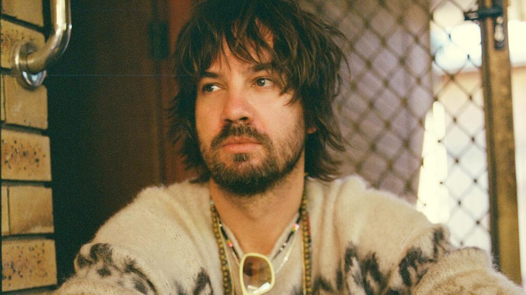 Australian musician Kevin Parker staring into the distance while sitting on a front porch.