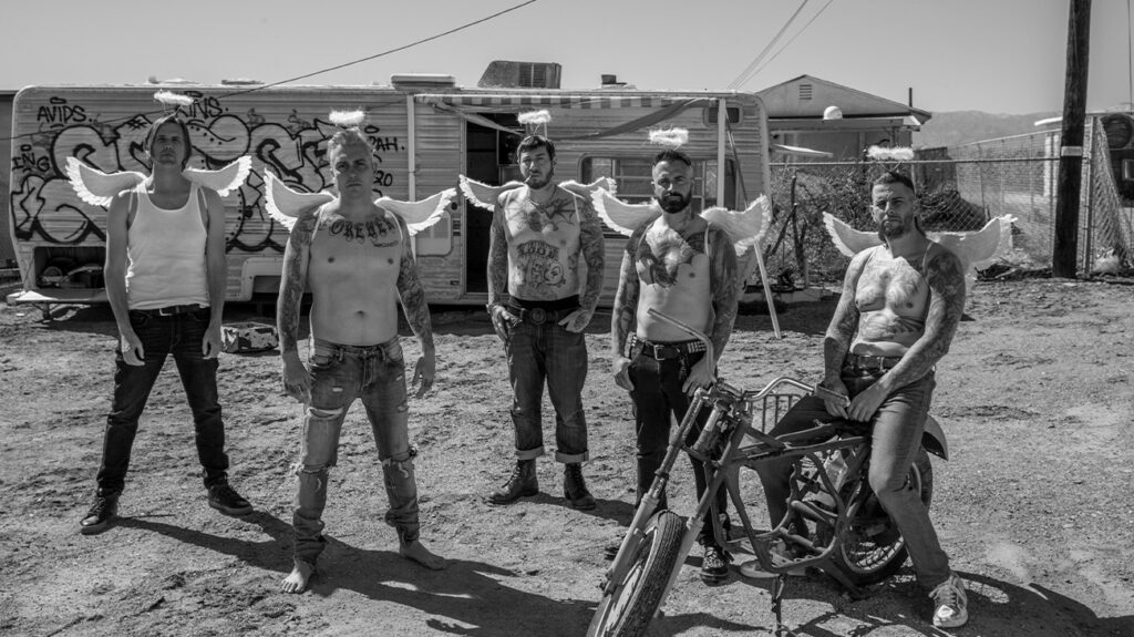 Avenged Sevenfold band members stand beside a motorcycle, posing together in casual attire.