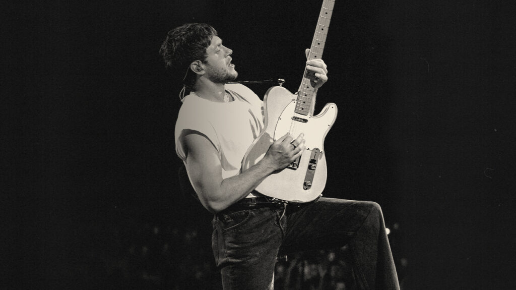 Black and white photo of Niall Horan performing with a guitar on stage.