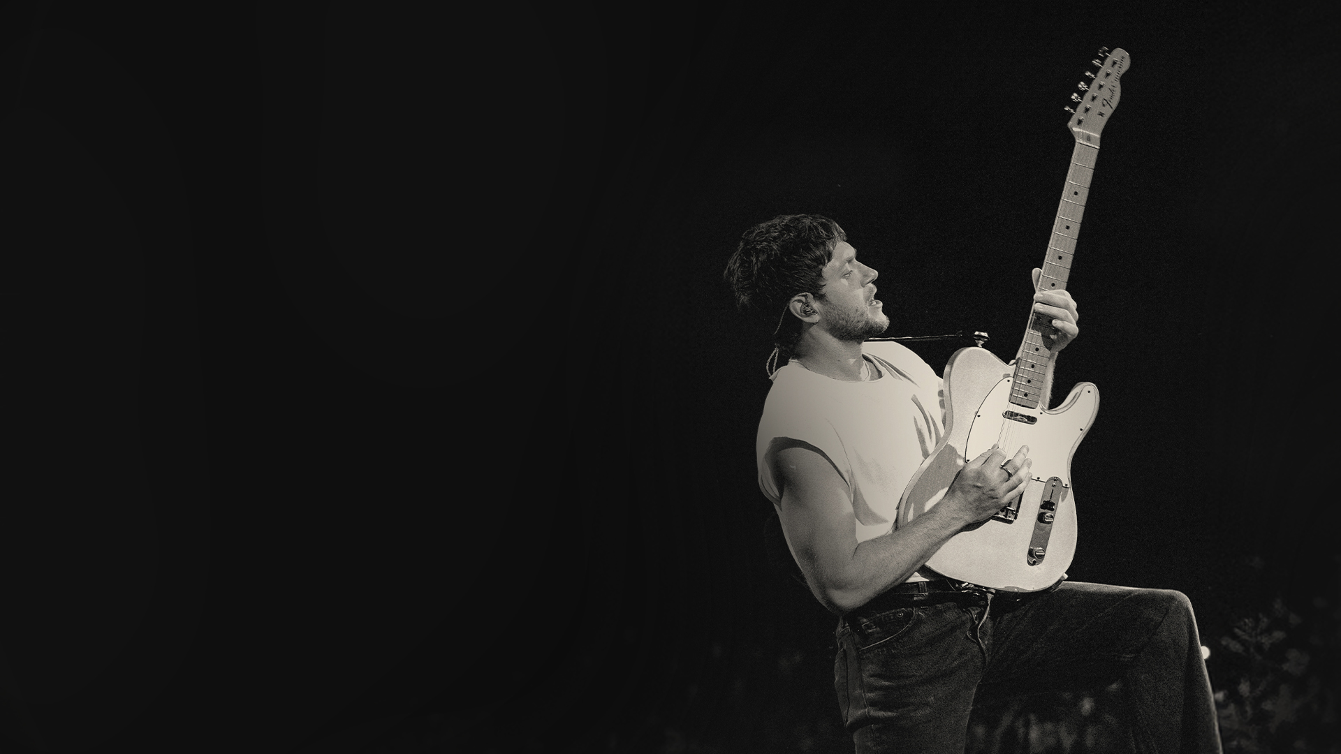 Black and white photo of Niall Horan performing with a guitar on stage.