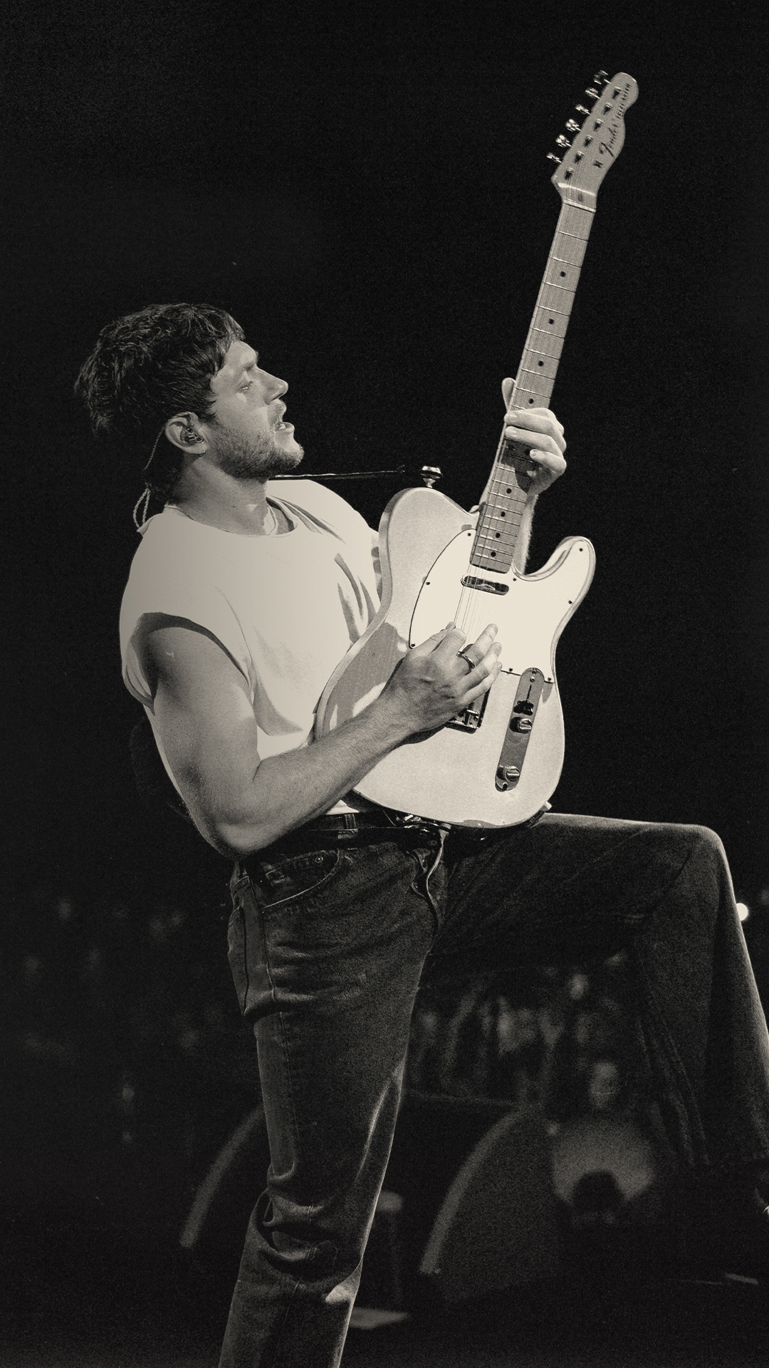 Black and white photo of Niall Horan performing with a guitar on stage.