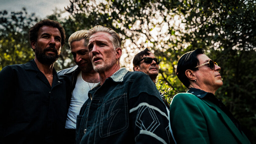 Queens of the Stone Age band members gathered and posing outdoors.