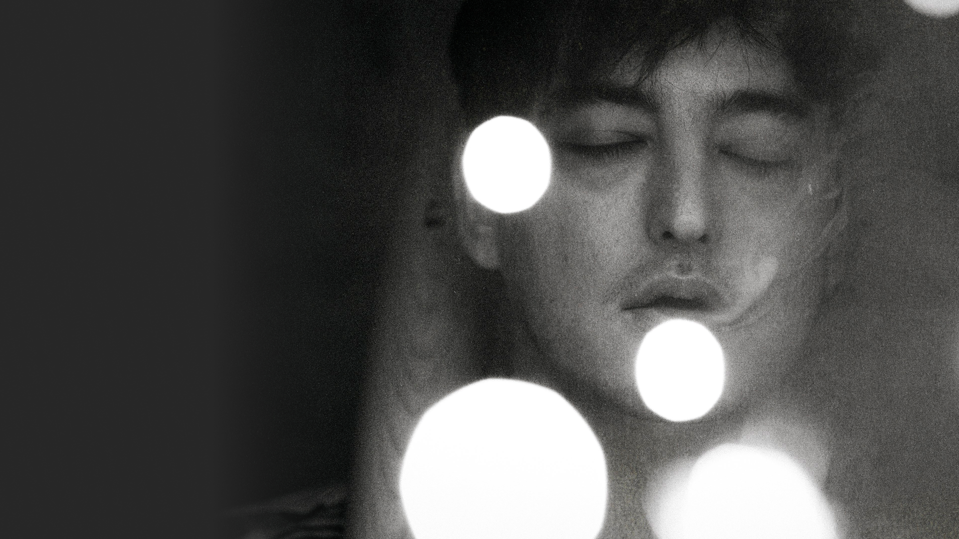 A close-up of singer Joji with his eyes closed, illuminated by a soft light.