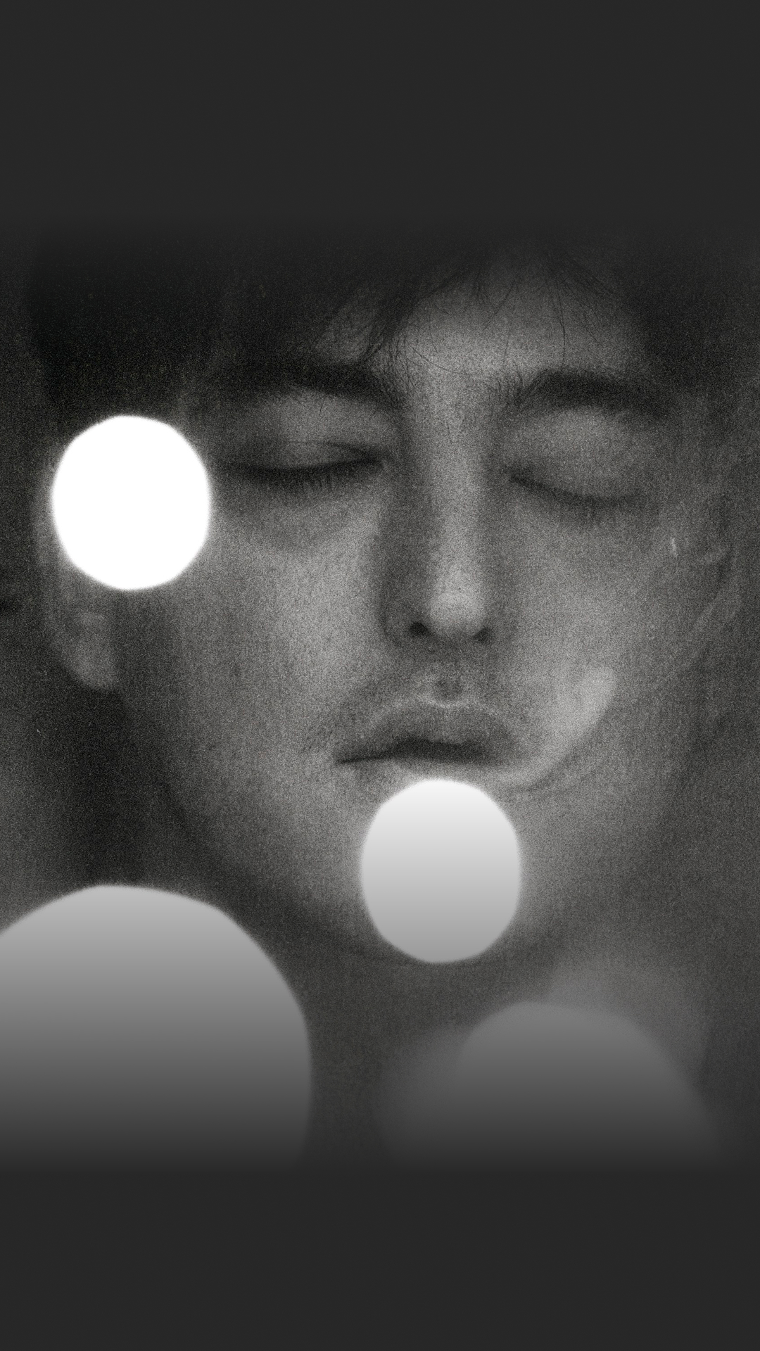 A close-up of singer Joji with his eyes closed, illuminated by a soft light.