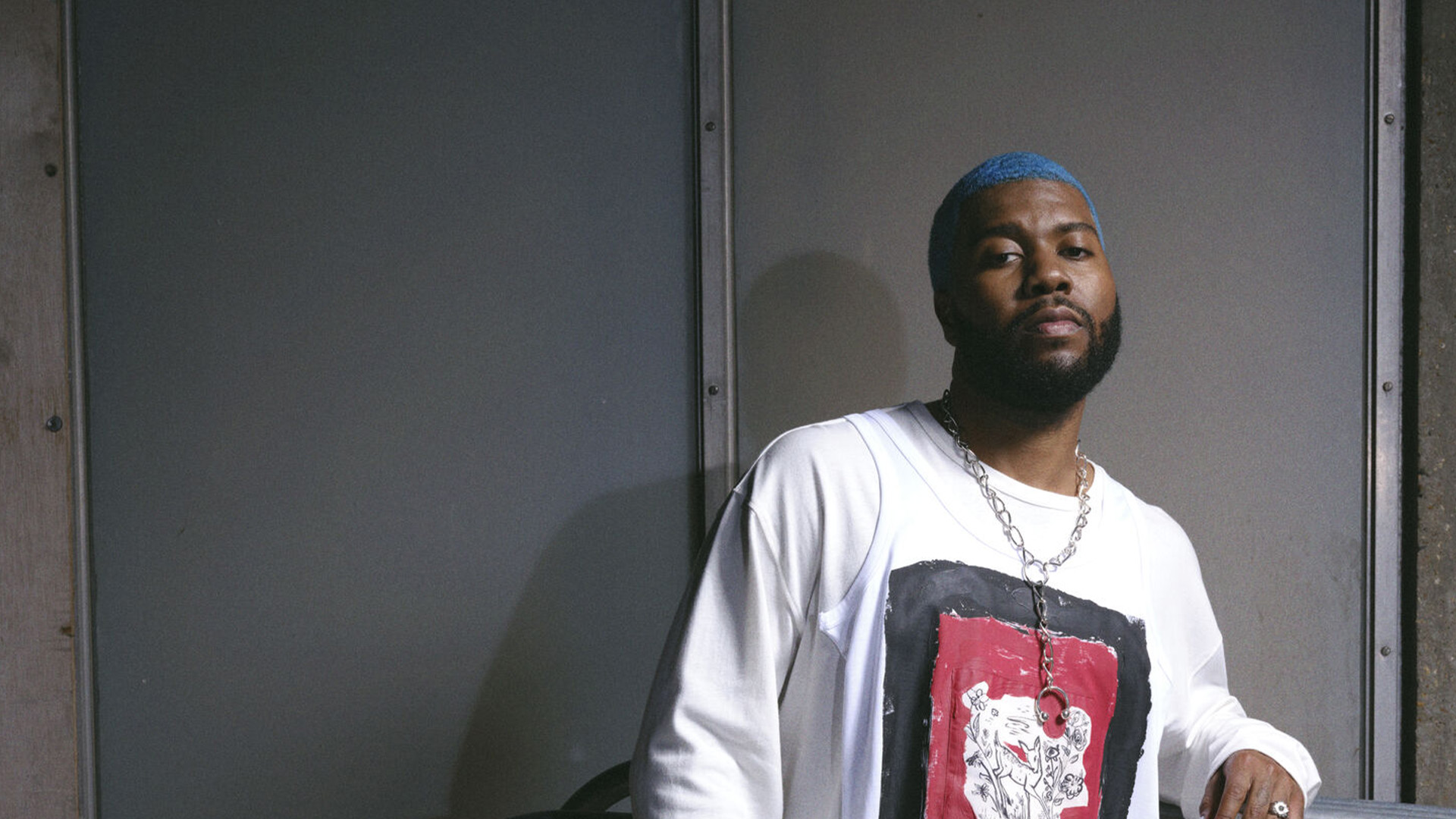 Khalid with a blue beard wearing a white shirt, smiling and looking directly at the camera.