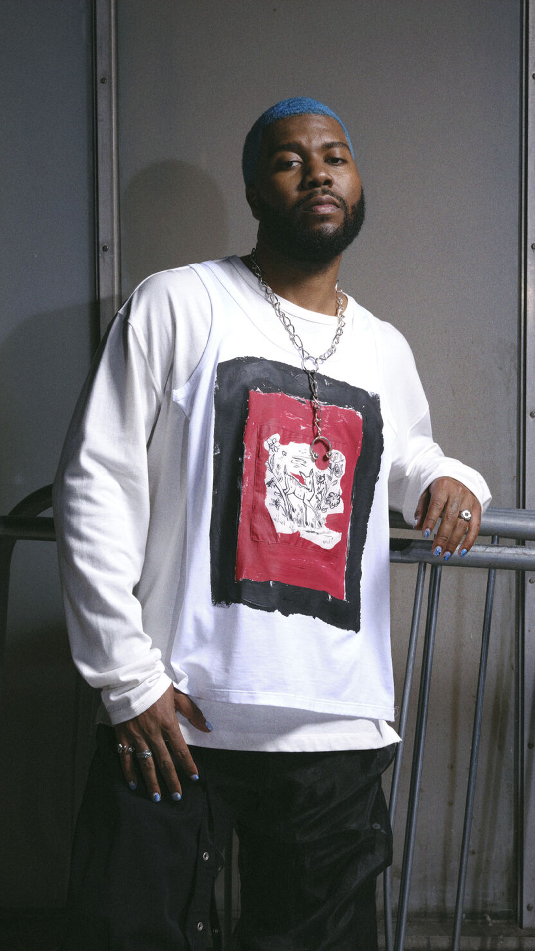 Khalid with a blue beard wearing a white shirt, smiling and looking directly at the camera.
